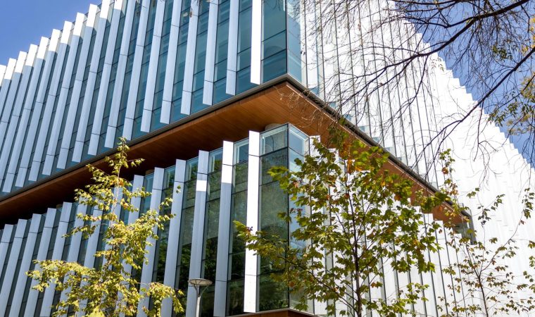 Contemporary glass-fronted office building with trees in urban setting on a sunny day.
