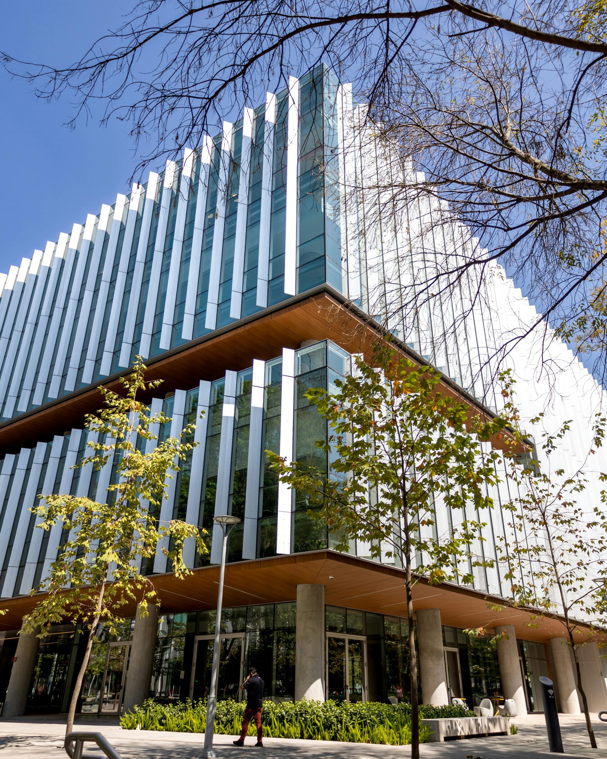 pexels-photo-15438557-15438557 Contemporary glass-fronted office building with trees in urban setting on a sunny day.